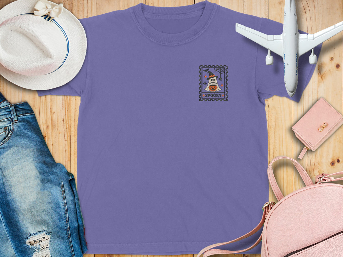 Lavender t-shirt with a ghost, pumpkin, and "SPOOKY" text on a postage stamp graphic.